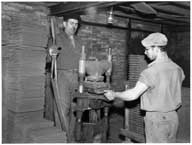 Atelier de façonnage : mise en forme des tuiles plates à la presse. A gauche, les galettes d'argiles en attente d'être pressées, à droite les tuiles pressées.- Photographie ancienne, 1956.