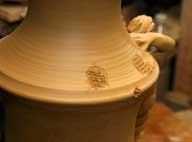 Reportage sur la fabrication d'un épi de faîtage dans l'atelier de poterie. Décoration de la base de l'épi : pose d'une pièce moulée, repères supérieurs.