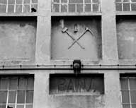 Bains-douches, dits salle des pendus, détail de l'élévation nord : marteau et pioche en sautoir sur une lanterne de mineur.- Photographie ancienne, 1992.